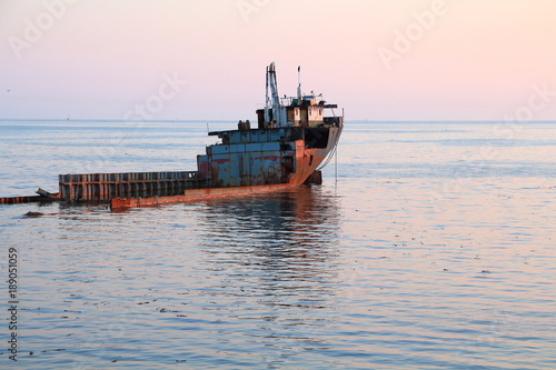 Unknown semi-submerged rusted and destroyed barge stranded in a bay