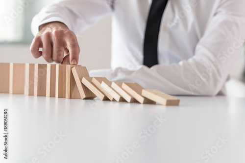 Businessman in white shirt stopping domino effect