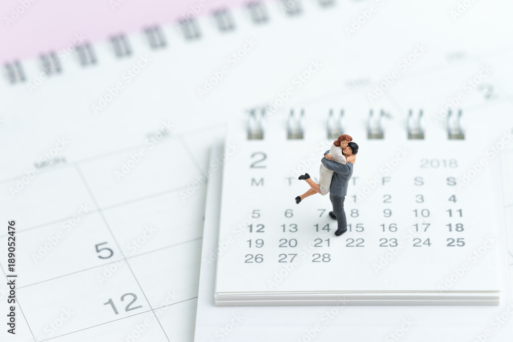 Valentines day celebration with lovely miniature couple standing on 14 Feb calendar on pink background Valentines day celebration with lovely miniature couple standing on 14 Feb calendar on pink background