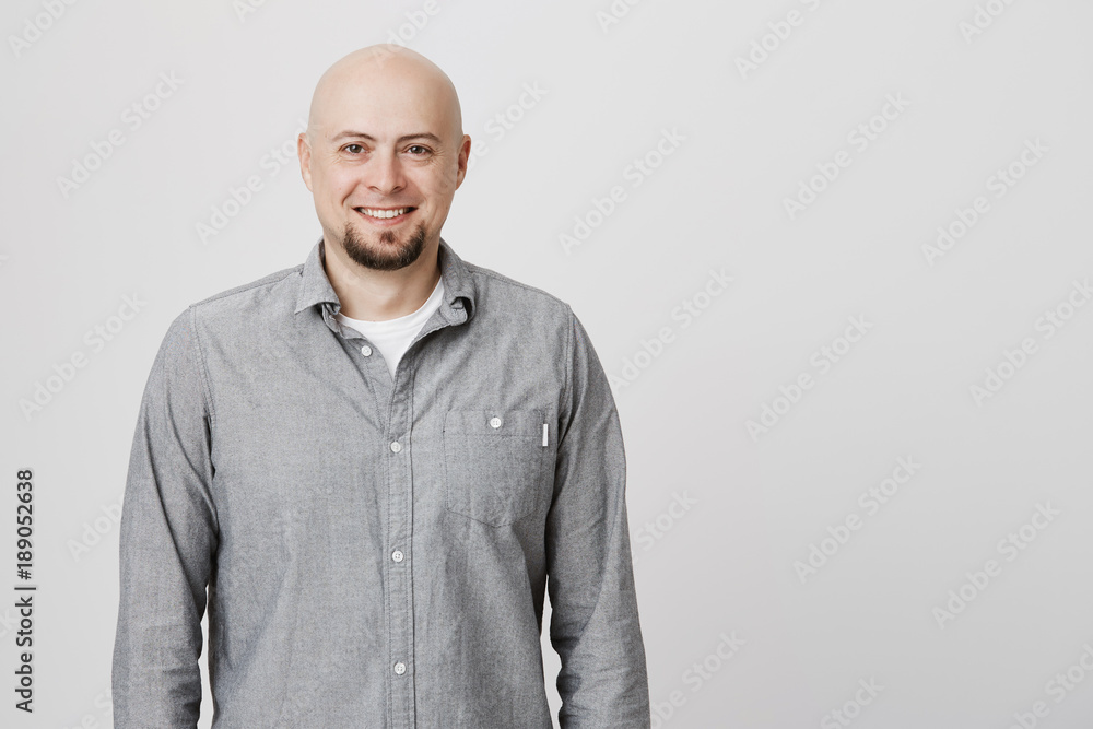 Portrait of bald adult man with beard standing casually over white background wearing gray shirt. Attractive male talking to his friend smiling cheerfully enjoying with their conversation. Portrait of bald adult man with beard standing casually over white background wearing gray shirt. Attractive male talking to his friend smiling cheerfully enjoying with their conversation.