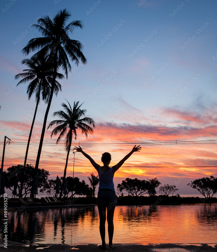 Silhouette of woman enjoying the sunrise view next to the swimming pool, summer travel concept