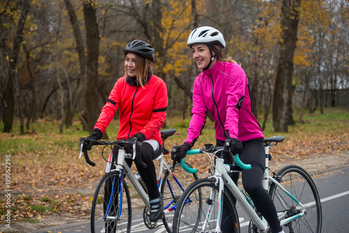 Two Young Smiling Female Cyclists with Road Bicycles Resting and in Park in Cold Autumn Day. Healthy Lifestyle.