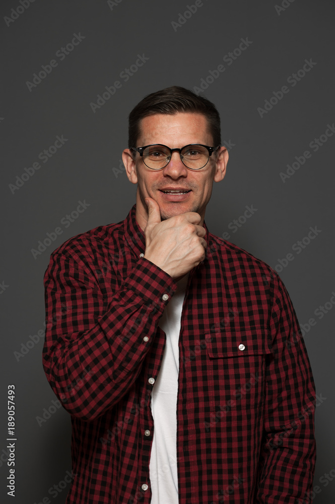 Fototapeta premium Close-up portrait of handsome positive young man with glasses and formal clothes looking at the camera on gray background