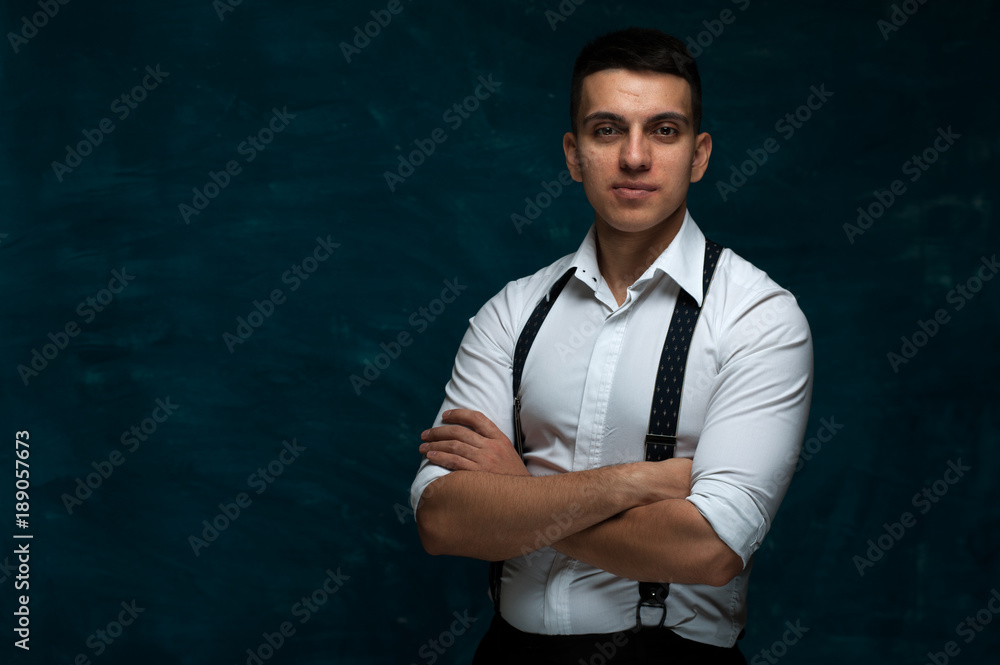 Portrait of serious young man in glasses and formal suit with suspenders on dark blue grunge background. Copyspace