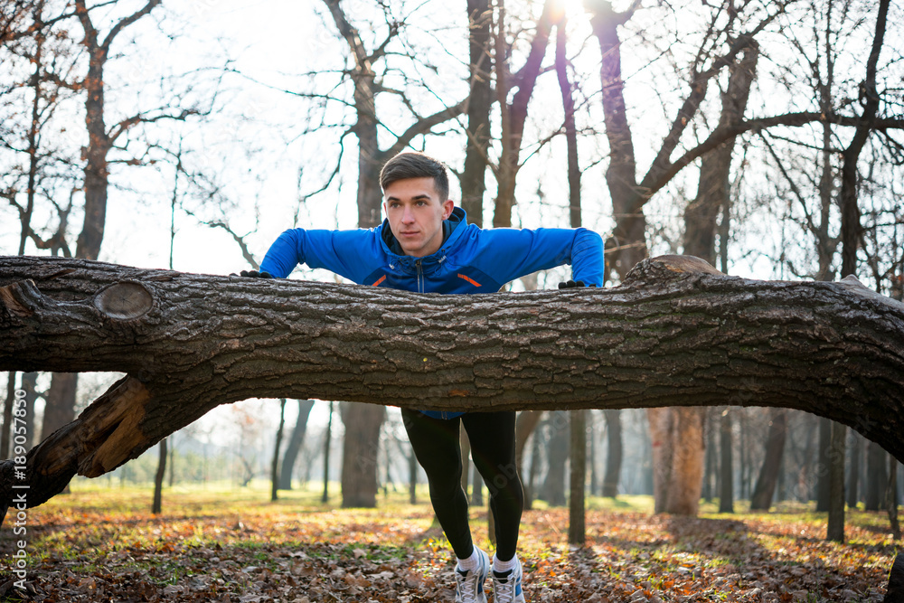 Male Runner Doing Push Up on the Log in the Park in Sunny Autumn Morning. Healthy Lifestyle and Sport Concept. Male Runner Doing Push Up on the Log in the Park in Sunny Autumn Morning. Healthy Lifestyle and Sport Concept.