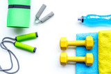 Do fintess in gym. Dumbbells, jump rope, expander, mat, water on white background top view copy space