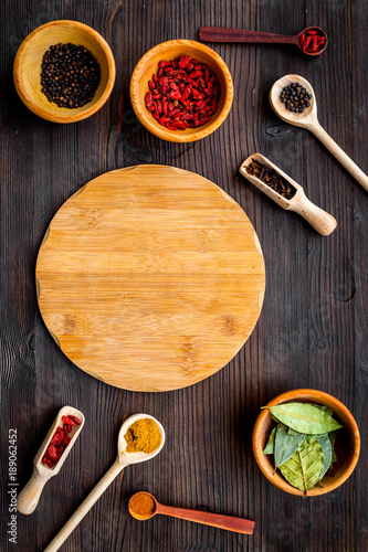 Make menu or write recipe. Mock up for menu or recipe. Wooden cutting board near spices and ingerdients in spoons and bowls on dark wooden background top view