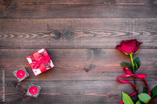 Fototapeta Naklejka Na Ścianę i Meble -  Prepare the prsesnts or surprise for Valentine's day. Red gift box near red rose on dark wooden background top view space for text