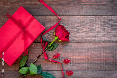 Fototapeta Naklejka Na Ścianę i Meble -  Prepare the prsesnts or surprise for Valentine's day. Red gift box near red rose on dark wooden background top view space for text