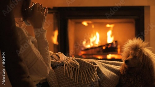 Young woman with her dog sitting at home by the fireplace and drinking a mug of cocoa .