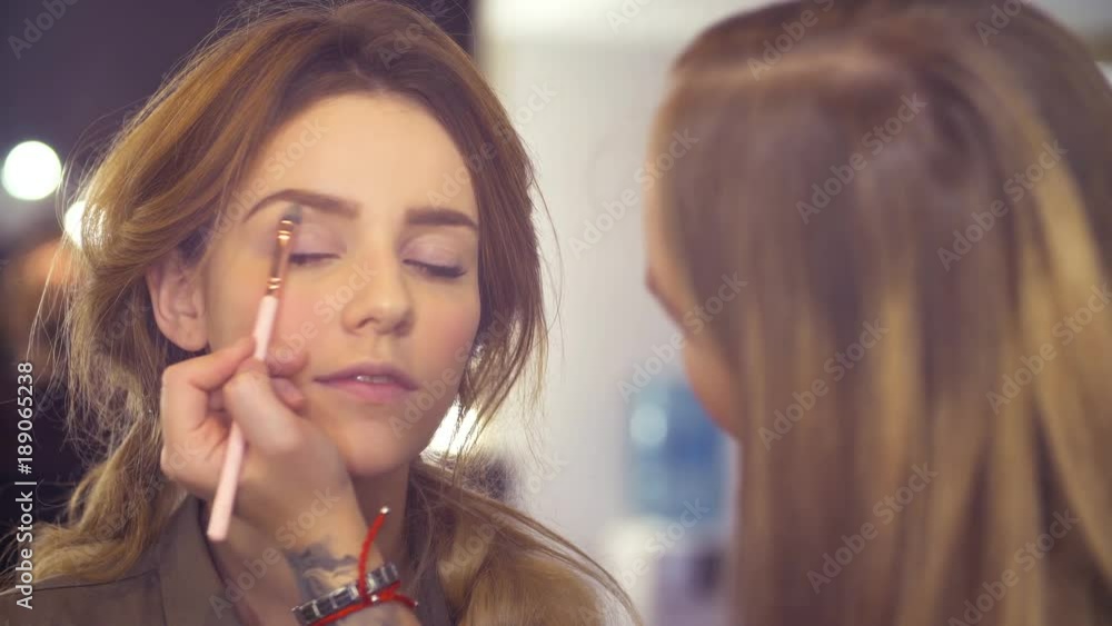 Portrait. Young attractive woman in visage studio. Professional makeup artist applying light powder around eyebrow with special brush Portrait. Young attractive woman in visage studio. Professional makeup artist applying light powder around eyebrow with special brush