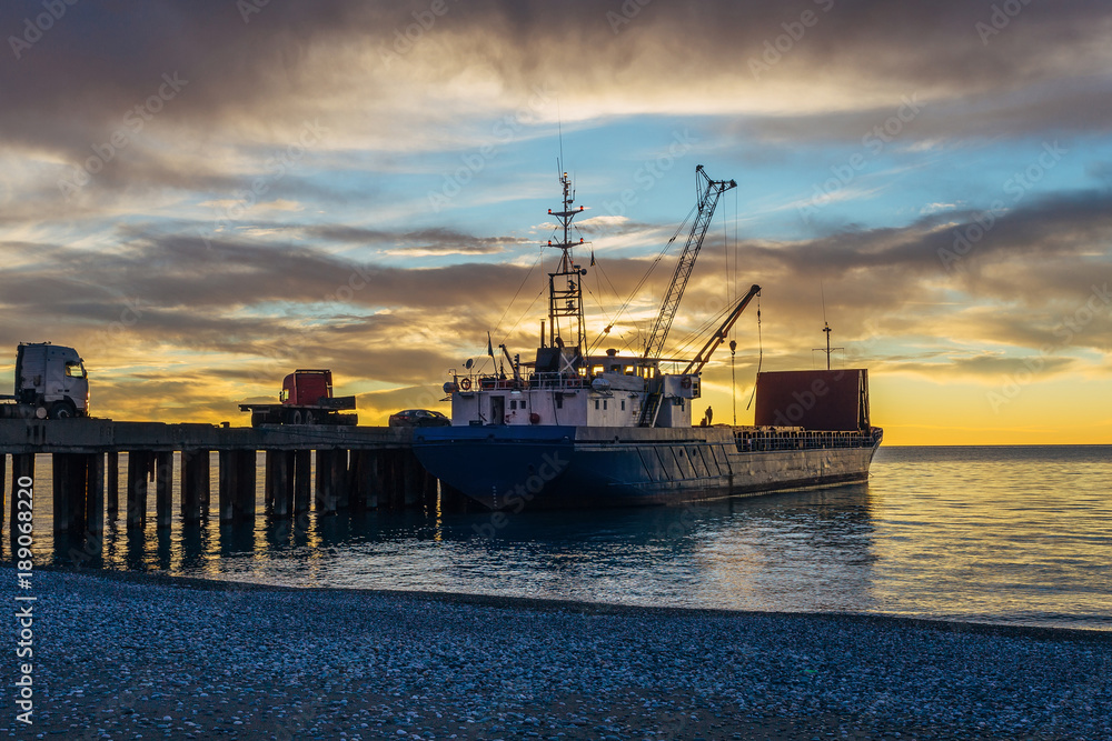Small port, cargo ship and cranes on the sunset