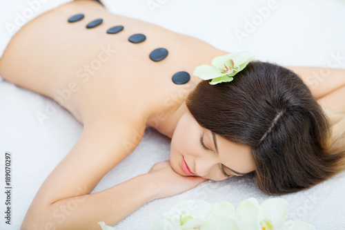 Beautiful woman relaxing in spa salon with hot stones on body