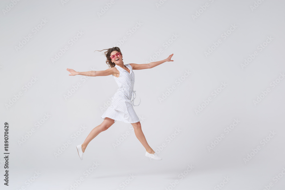 Playful girl gesturing and smiling while jumping against background