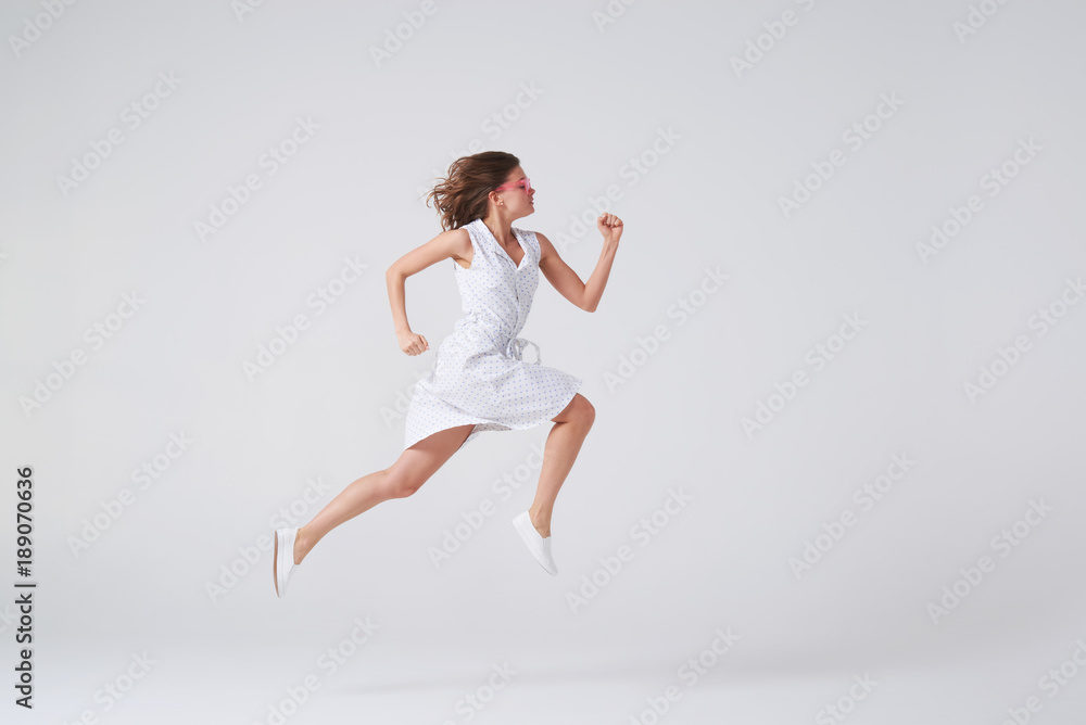 Joyous girl in dress jumping up in air over background in studio