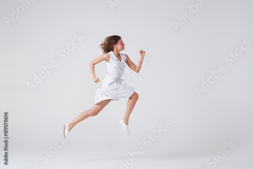 Joyous girl in dress jumping up in air over background in studio