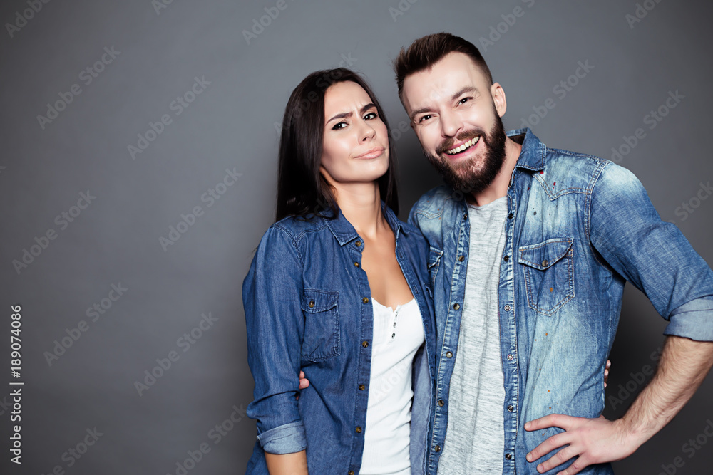 Beautiful and happy young couple in love or family in casual wear having fun and making fun of each other and posing on a gray background isolated.