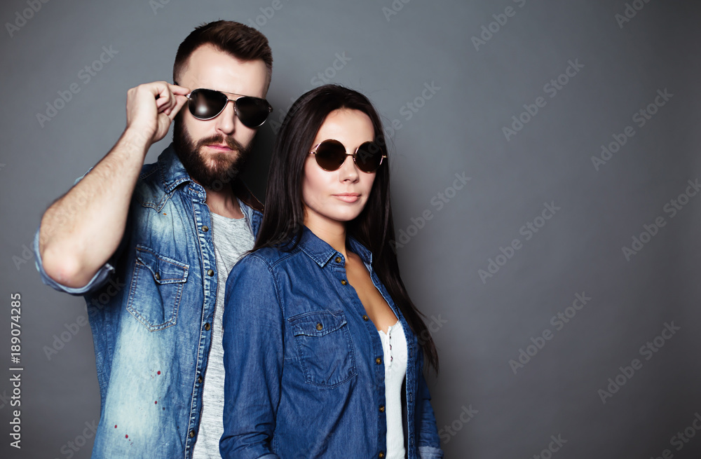 A young stylish fashion couple in casual clothes with black glasses look at the camera on a gray background. A young stylish fashion couple in casual clothes with black glasses look at the camera on a gray background.