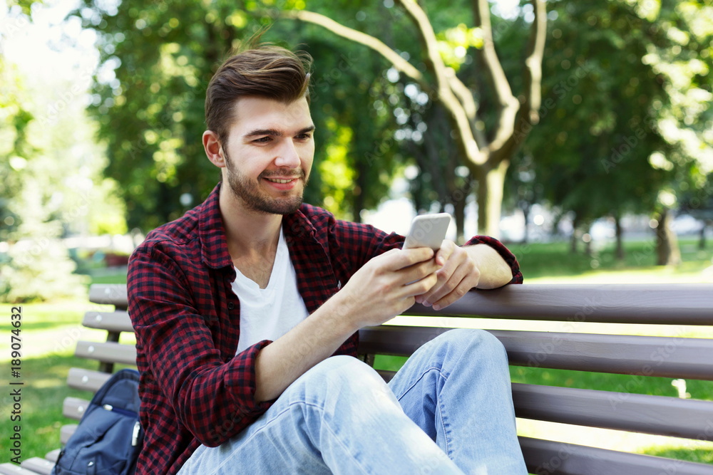 Handsome man sitting and using smartphone outdoors Handsome man sitting and using smartphone outdoors