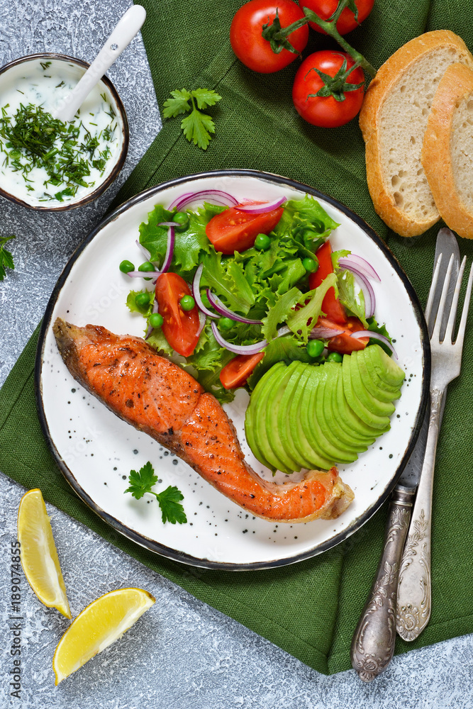 Plakat Food background. Baked trout with garnish of vegetable salad and avocado, with cream sauce on a concrete background.
