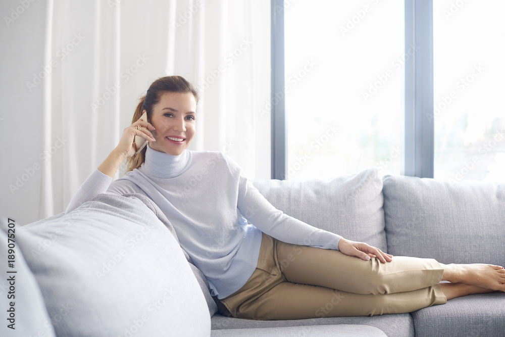 Attractive mature woman talking with somebody on mobile phone while sitting on couch at home Attractive mature woman talking with somebody on mobile phone while sitting on couch at home