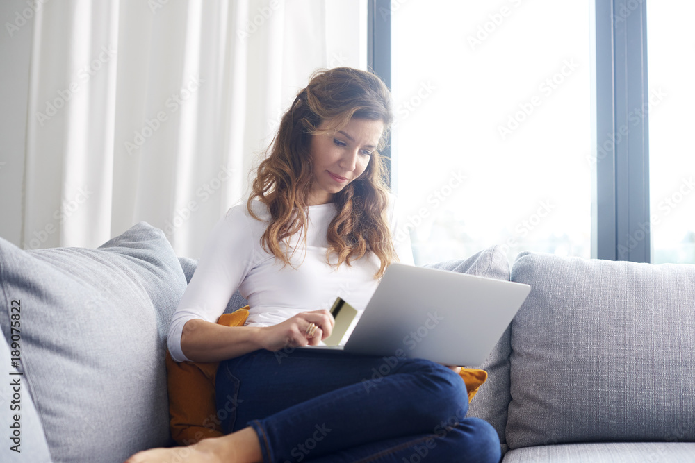 Banking from home is comfy. A woman sitting on sofa and looking thoughtful while shopping online with her credit card. Banking from home is comfy. A woman sitting on sofa and looking thoughtful while shopping online with her credit card.