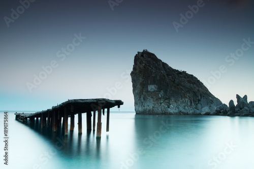 Old decaying and dilapidated pier with smooth sea and rock photo