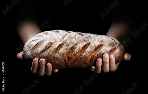 A loaf of freshly baked bread in the hands of a baker on a black background.