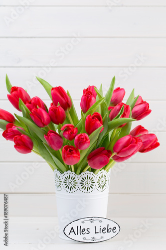 Fresh red tulip flowers bouquet on shelf in front of wooden wall.