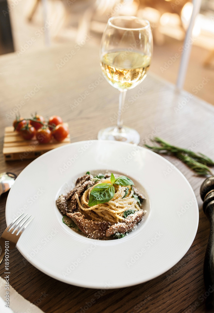Italian pasta with meat, basil and Parmesan with a glass of wine on a wooden table