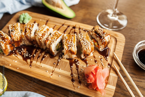 Japanese sushi rolls with wasabi, ginger soy sauce and chopsticks and a glass of wine on a wooden board