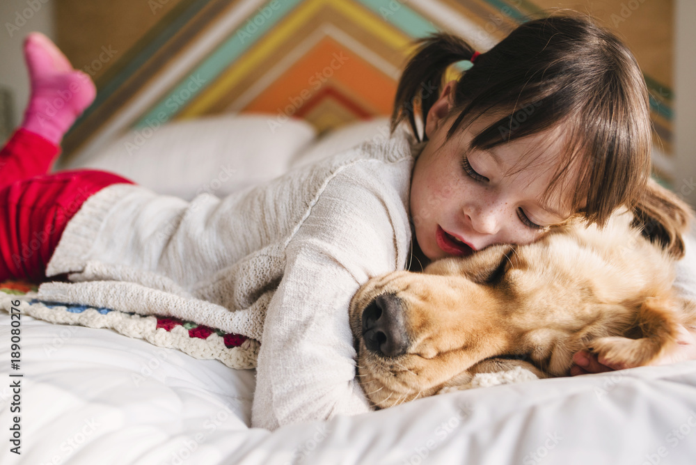 Girl lying on a bed with her golden retriever dog Stock Photo | Adobe Stock