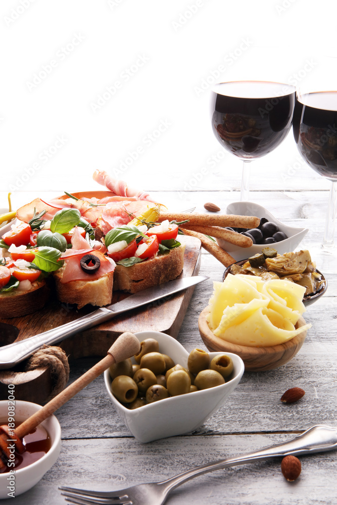 Italian antipasti wine snacks set. Cheese variety, Mediterranean olives, pickles, Prosciutto di Parma, tomatoes, artichokes and wine in glasses Italian antipasti wine snacks set. Cheese variety, Mediterranean olives, pickles, Prosciutto di Parma, tomatoes, artichokes and wine in glasses