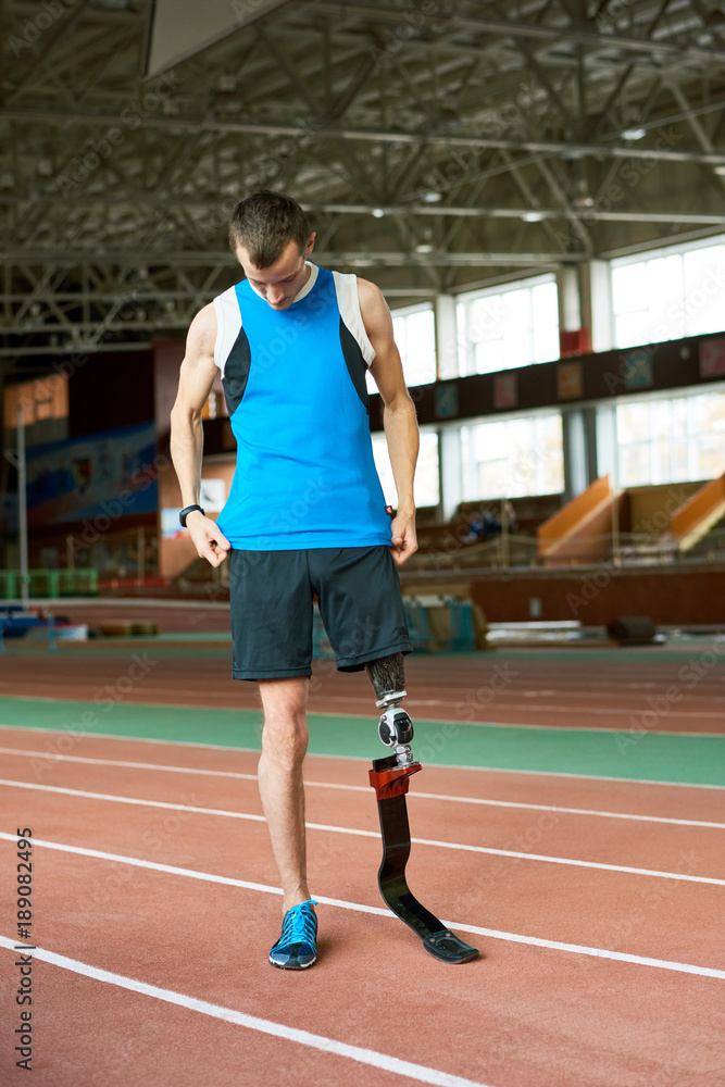 Full length portrait of young amputee athlete standing on track before running practice in modern indoor stadium  copy space