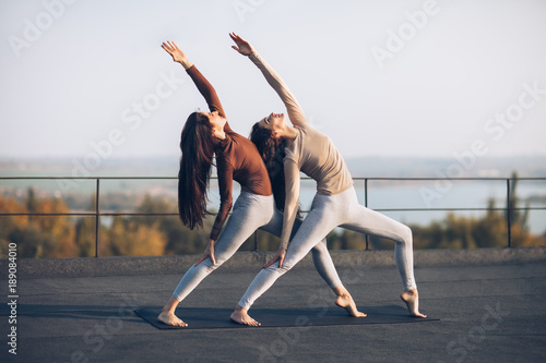 Two beautiful women perform double pose warrior with raised hand