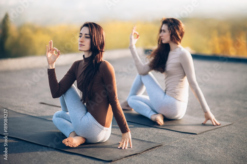 Two young women doing yoga asana half lord of the fishes pose on the roof outdoor photo