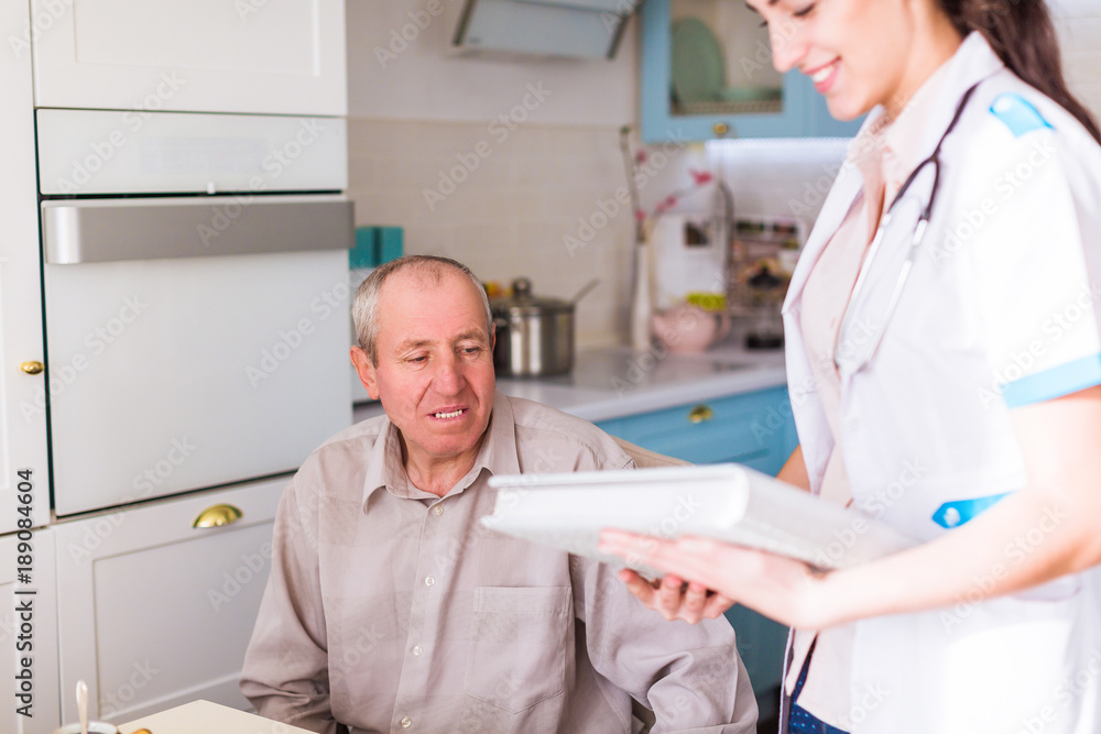 Obraz premium The young doctor standing near ill old man and holding photo album in hands at home