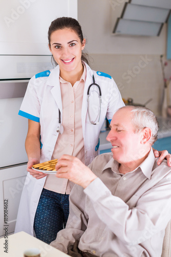 The happy young doctor standing near old, ill man and giving cookies him in the kitchen