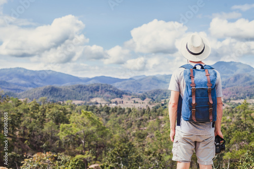 summer trekking in the mountains, tourist hiker travels outdoors, hipster with camera and backpack looking at panoramic landscape