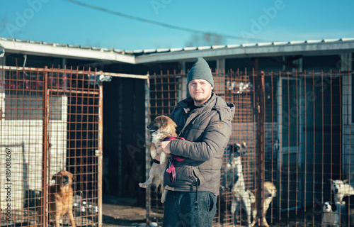 Sticker The dog trainer smiles while holds a stray dog in his arms while carrying it in his cage in the winter sun light
