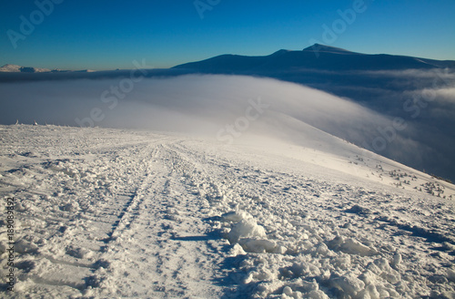 Winter snowy landscape of mountains in background of blue sunny sky