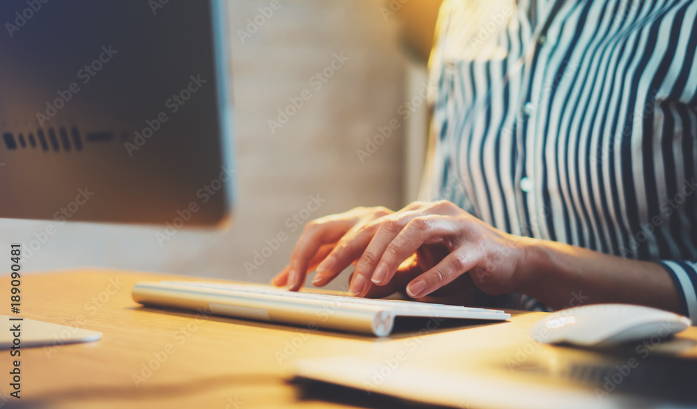 Fototapeta premium Businesswomen working at office with monitor computer, young hipster manager typing on keyboard, closeup finger female hands texting message, work process concept in workspace, night atmospheric .