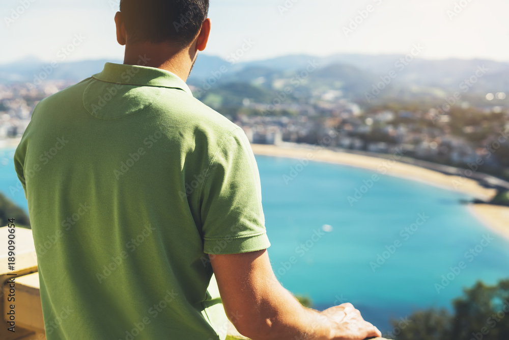 Fototapeta premium Hipster młody człowiek patrząc na taras widokowy podczas wakacji w San Sebastian, ciesząc się widokiem na morze na górze i oceanie, podróżnik turystyczny na tle panoramiczny widok na miasto