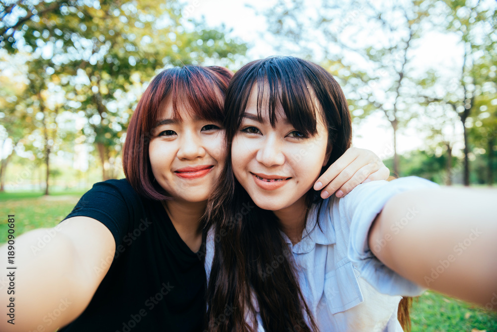 Fototapeta premium Two beautiful happy young asian women friends having fun together at park and taking a selfie. Happy hipster young asian girls smiling and looking at camera. Lifestyle and friendship concepts.