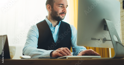 Bearded young businessman working on modern office at night. Consultant man thinking looking in monitor computer. Manager typing on keyboard in coworking workplace, startup project concept in studio photo