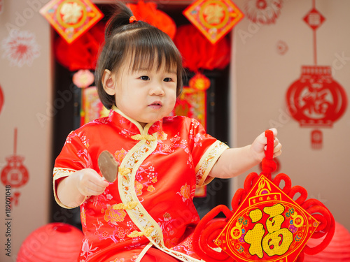 Chinese baby girl  with traditional dressing up and "FU" means "lucky" greeting card.some "FU" means "lucky"greeting card on the wall