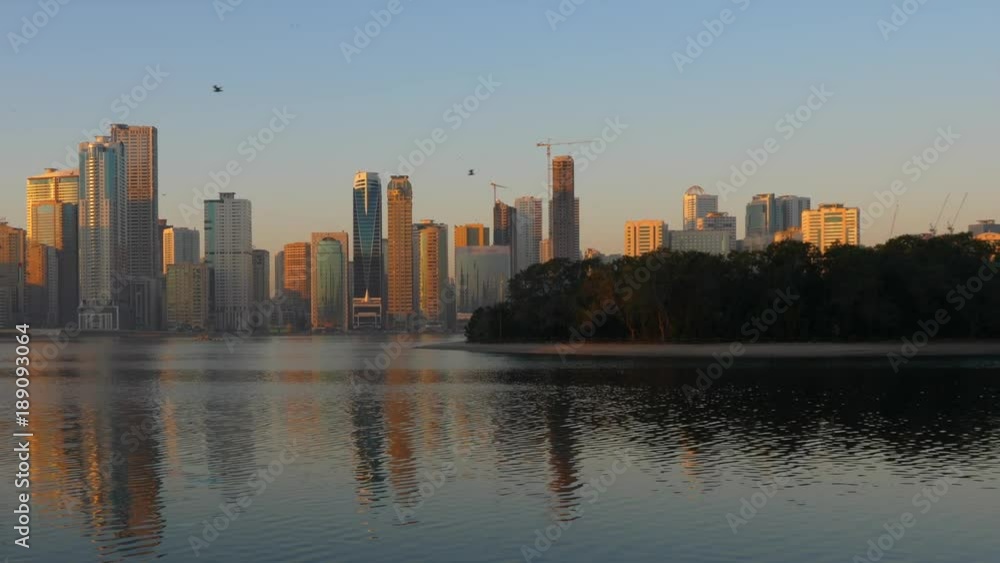 Walk along embankment at Khalid lake in Sharjah, UAE. Skyline with skyscrapers. Al Noor Island at water. Morning city landscape scene. Walk along embankment at Khalid lake in Sharjah, UAE. Skyline with skyscrapers. Al Noor Island at water. Morning city landscape scene.