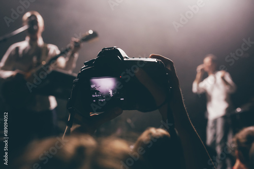 Someone's dslr camera with the video record mode on a concert with the live view picture on a screen. Music band on a stage as an object of shooting photo