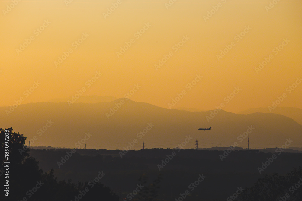 A low-flying plane and mountains are silhouetted at dusk.