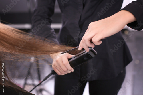 Professional stylist straightening woman's hair in salon, closeup
